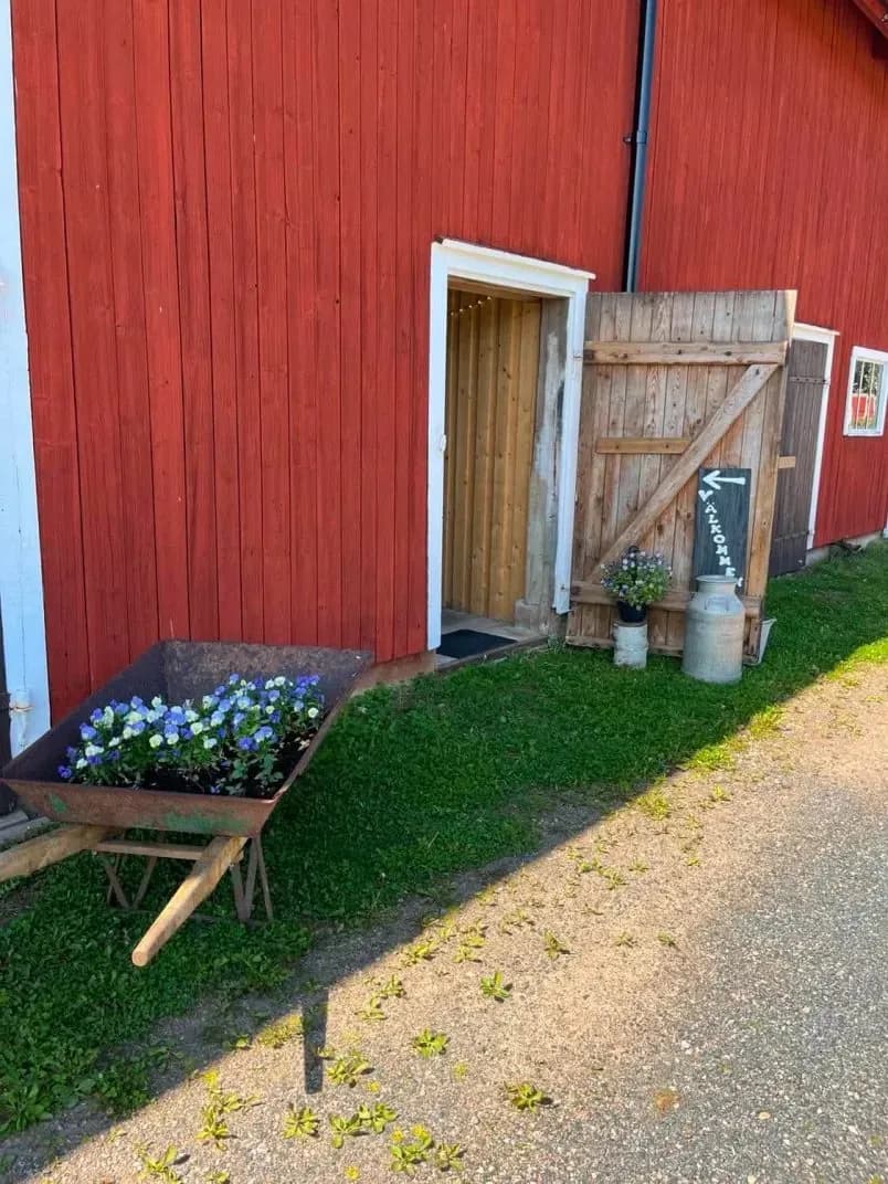 Rödmålad ladugård på landet med blomsterlåda och handmålad välkomstskylt vid entrén